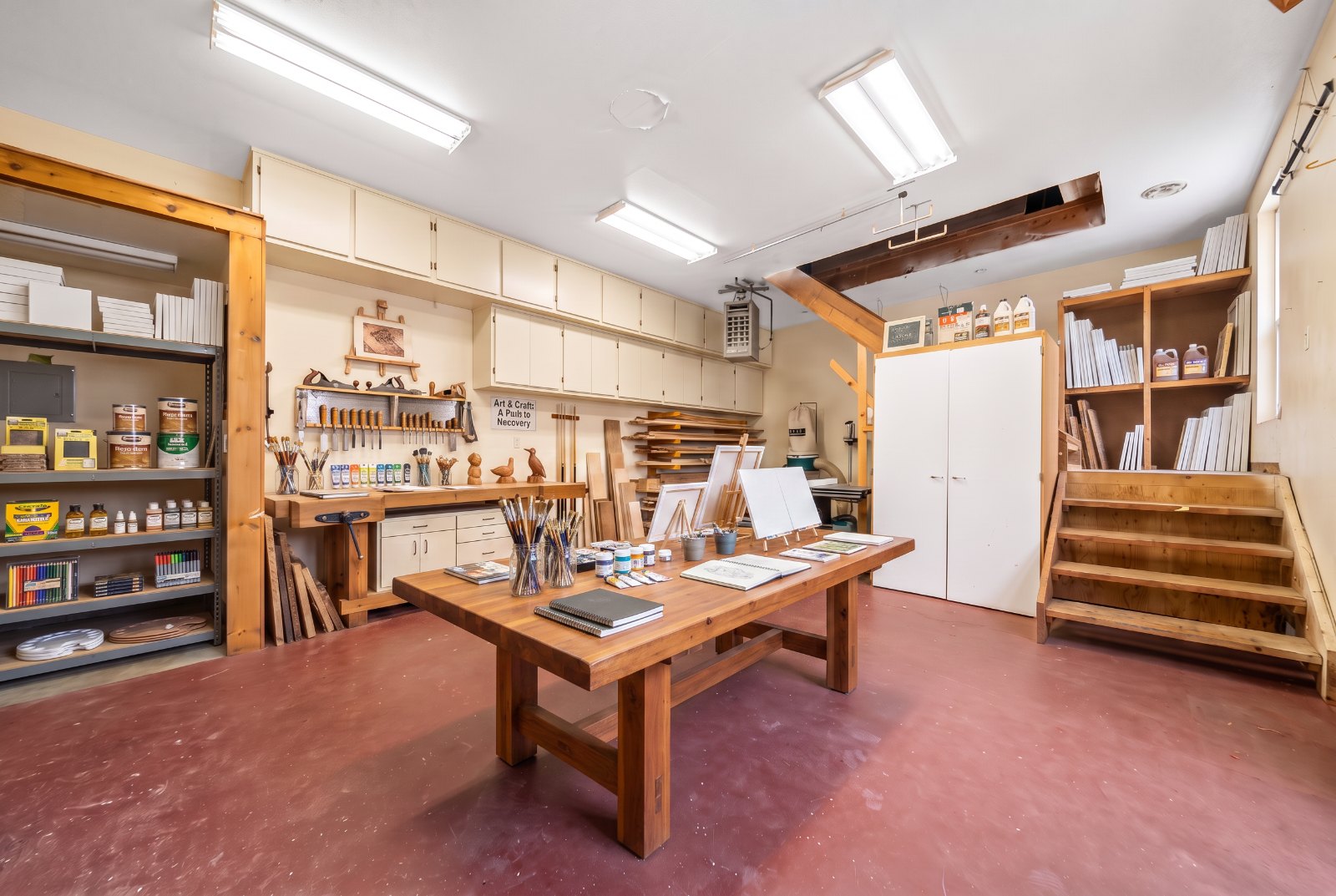 Art and woodworking studio with a large shared worktable, easels, and supplies
